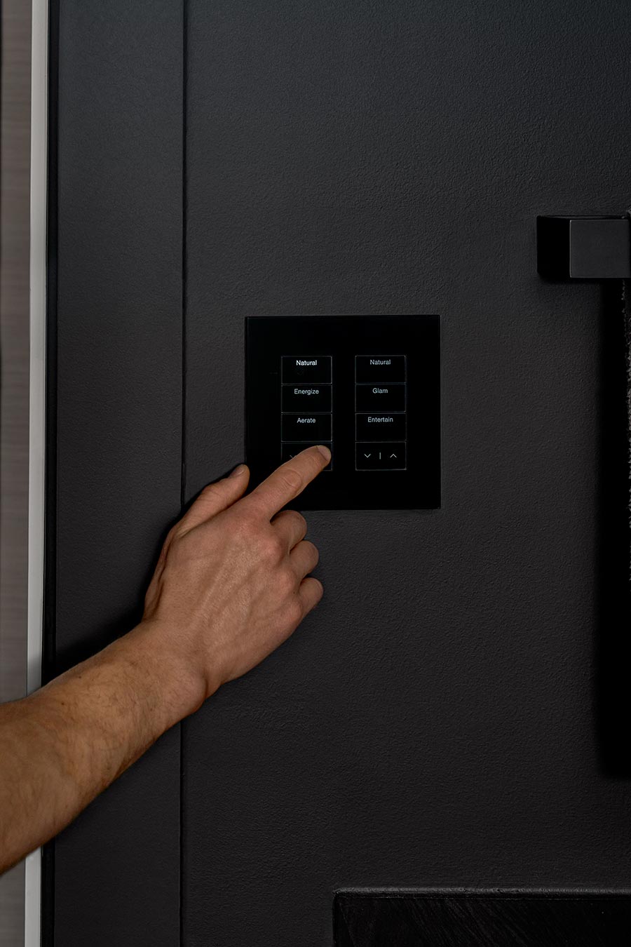 Close-up of a hand pressing a black smart lighting keypad on a dark wall