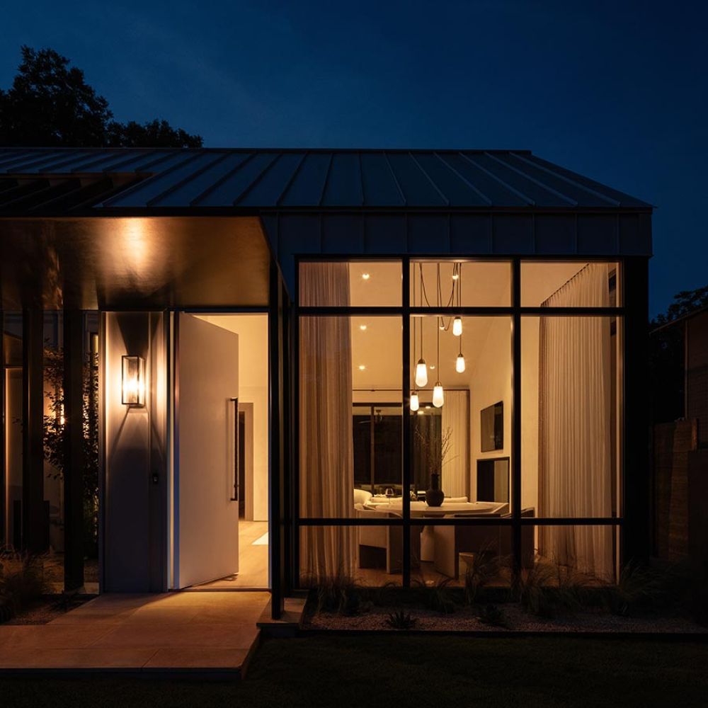 Modern house entrance at night with warm interior pendant lighting and large windows